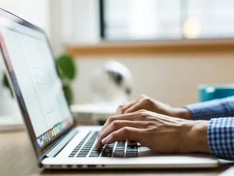 Hands typing on a laptop at a bright desk